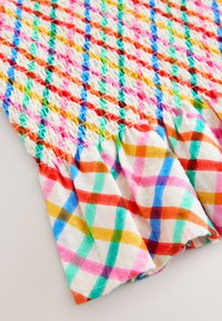 Tissu blanc avec motif à carreaux diagonaux multicolores et couture smockée créant un effet texturé et froncé près du bord supérieur.