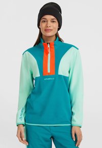 Teal-Fleece-Pullover mit einem halben Reißverschlusskragen, orangefarbenen Akzenten und weißem Logo. Verfügt über kontrastierende Ärmel und ein "Polartec"-Detail an den Bündchen.
