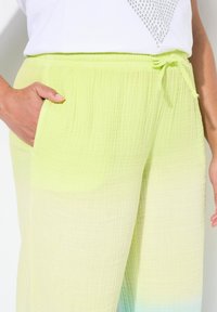 Lichtgroene, textuurachtige broek met een elastische tailleband en trekkoord. Beschikt over zijzakken en een geleidelijke blauwe ombre-effect aan de onderrand.