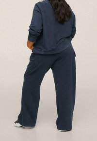 Sweatshirt bleu foncé et pantalon large assorti en tissu doux, avec des coutures visibles et des poches latérales sur le pantalon.