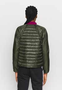 Grön puffjacka med horisontell quiltning på baksidan, slät textur och design med raglanärm. Kontrastkrage och åtsittande ärmmuddar.