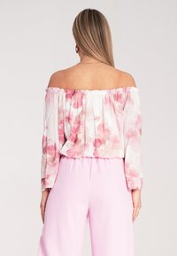 Kwiatowa bluzka bez ramiączek z różowymi i białymi wzorami w akwareli; zestawiona z jasnoróżowymi spodniami o wysokim stanie. Długie rękawy z elastycznymi mankietami.