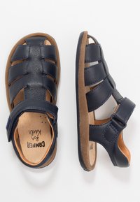 Granatowe skórzane sandały z odkrytymi palcami, regulowanym paskiem i brązową teksturowaną wkładką. Wyposażone w wiele wentylowanych pasków dla zapewnienia oddychalności.