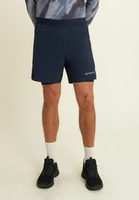 Pantaloni sportivi navy con texture liscia, vita elastica, tasche laterali con zip e dettagli del logo discreti sull'orlo.