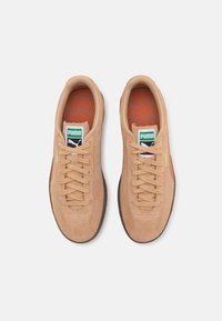 Pár béžových semišových tenisek Puma s oranžovými akcenty, zeleným a bílým logem Puma na jazycích a oranžovými vzorovanými vložkami, pohled zeshora.