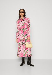 Long, button-up dress featuring a vibrant floral pattern in pink, green, and black. Paired with black knee-high boots and a small yellow handbag.