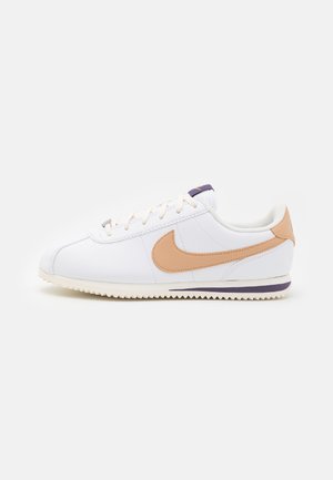 Weißer Nike-Sneaker mit beigem Swoosh, weißen Schnürsenkeln und profiliertem Profil auf hellem Hintergrund, Seitenansicht des rechten Schuhs.