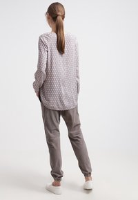 Blouse à motifs gris clair avec des manches longues et un col rond, associée à un pantalon gris ample et des baskets blanches. Texture de tissu lisse.