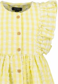 Robe à carreaux jaunes et blancs avec des manches volantées, des boutons en bois et une taille froncée. Tissu doux et léger avec une finition texturée.