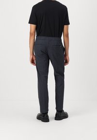 Grå mönstrade byxor med en avslappnad passform, elastisk midja och bakfickor. Kombineras med en svart kortärmad skjorta och svarta skor.