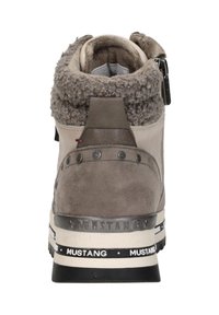 Grijze suède enkellaars met een fuzzy kraag, decoratieve hardware en logo-banddetails rondom de zool. Zipper aan de zijkant voor eenvoudig aan- en uittrekken.