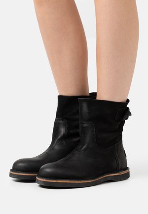 Botas de tobillo de cuero negro con un acabado suave, que cuentan con un diseño de solapa, una suela de goma plana y un pequeño detalle de hebilla lateral.