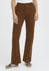 Brown corduroy flared pants with a textured surface, front pockets, and a button closure, worn with gray and white sneakers.