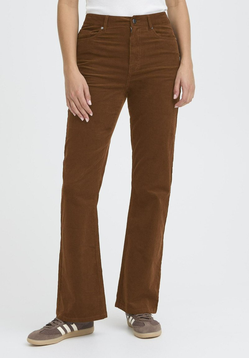 Brown corduroy flared pants with a textured surface, front pockets, and a button closure, worn with gray and white sneakers.