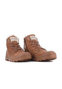 Bottes en cuir marron avec doublure en fausse fourrure, lacées sur le devant, fermeture éclair sur le côté, et semelles en caoutchouc texturé avec une adhérence à motif. Étiquette PALLADIUM sur la languette.
