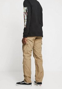 Musta pitkähiha paita, jossa värikkäät kuviot hihassa, yhdistetty ruskeisiin cargo-housuihin, joissa on sivutaskut ja normaali istuvuus.