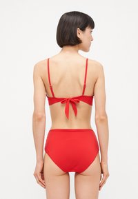 Rdeči bikini komplet z vezano zadaj in nastavljivimi naramnicami. Hlačke z visokim pasom z gladko teksturo in minimalističnim dizajnom.