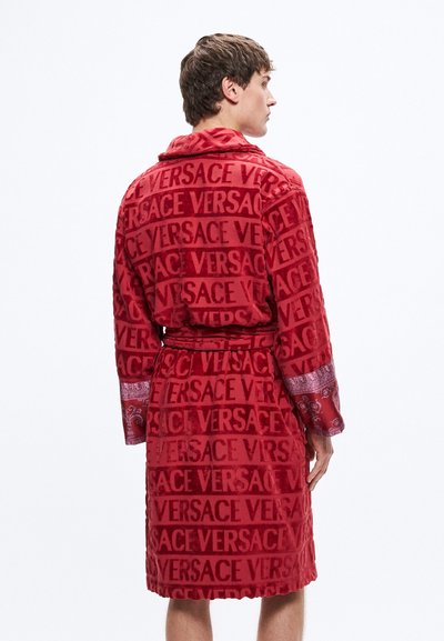 Červený plyšový župan se vzorem celoplošného loga "VERSACE", s kontrastními vzory na manžetách a zavazovacím páskem.