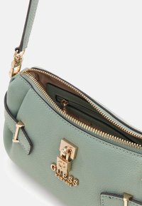 Miętowa skórzana torebka z złotymi okuciami, zamkiem błyskawicznym i podszewką wewnętrzną. Charakteryzuje się dekoracyjnymi akcentami i usztywnionym kształtem.