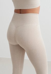 Leggings beige acanalados con cintura alta y diseño sin costuras. La tela es suave con un acabado texturizado que presenta rayas verticales a lo largo de toda la prenda.