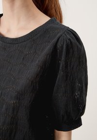 Sort top med rund halsudskæring og pufærmer. Fremstillet af tekstureret stof med zigzag-mønstre og en let løs pasform.