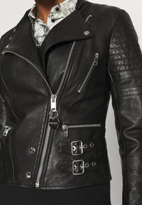 Svart läderbikerjacka med silverdragkedjor, knappstängning, kviltade axlar och justerbara sidspännen.