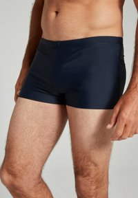 Marineblaue Schwimmshorts aus glattem, dehnbarem Material; figurschnitt; Oberschenkellänge; elastischer Bund; minimaler Nahtanteil.