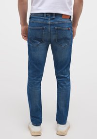 Jeans de mezclilla azul con un ajuste slim, que cuentan con bolsillos traseros, una etiqueta de cuero en la cintura y un sutil desgaste a lo largo de las piernas.