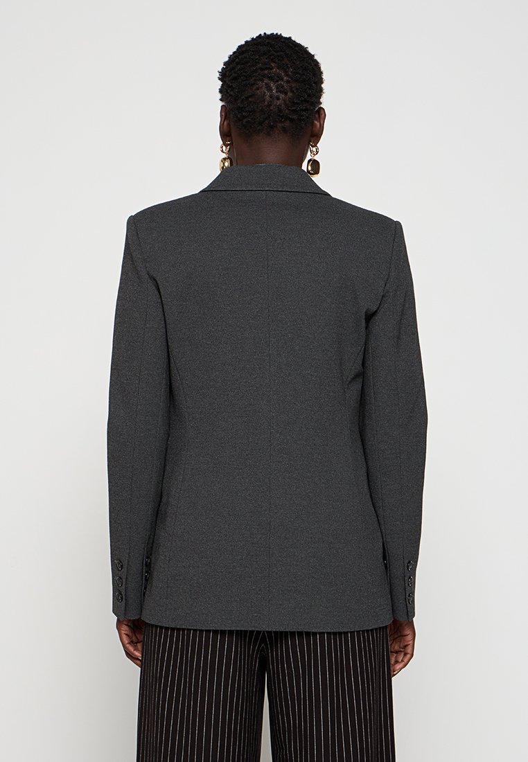 Blazer grigio con un design strutturato, colletto a punta e polsini abbottonati, realizzato in tessuto testurizzato, con una cucitura centrale sul retro.