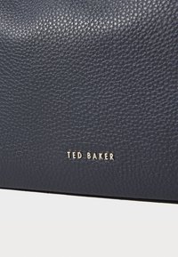 Marine strukturert skinnhåndveske med en glatt overflate. Har en gull "TED BAKER"-logo i nedre høyre hjørne.