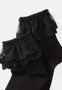 Calcetines negros con un borde de encaje fruncido y patrones florales, hechos de un material suave con una textura lisa.