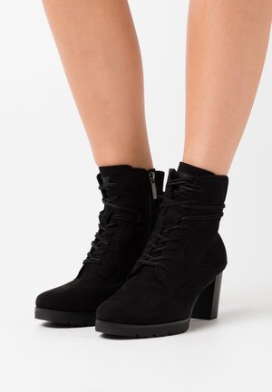 Bottines en daim noir avec un talon bloc, un design à lacets et une fermeture éclair latérale. Caractérisées par une texture lisse et des motifs de couture simples.