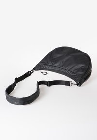 Schwarze halbkreisförmige Umhängetasche mit verstellbarem Riemen und Reißverschluss, liegend auf einer weißen Oberfläche.