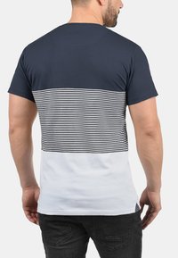Camiseta azul marino con un patrón a rayas horizontales en blanco y negro en la sección superior y una sección inferior sólida blanca.