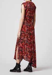 Abito maxi con stampa leopardata rossa e nera, maniche corte, spacchi laterali alti e una linea fluida. Indossato con stivali neri con lacci.