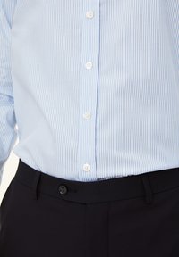 Camicia a righe blu chiaro e bianca con design a bottoni, abbinata a pantaloni neri con chiusura a un bottone.