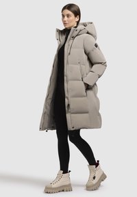 Garšs, gaiši pelēks pūkains mētelis ar kapuci, ar rāvējslēdzēja priekšpusi, sānu kabatām un quilted tekstūru, saskaņots ar bežām masīvām zābakām.