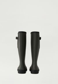 Botas de goma verdes hasta la rodilla con ribete negro, que cuentan con una superficie texturizada y una correa ajustable en el lateral, diseñadas para la durabilidad y la comodidad.