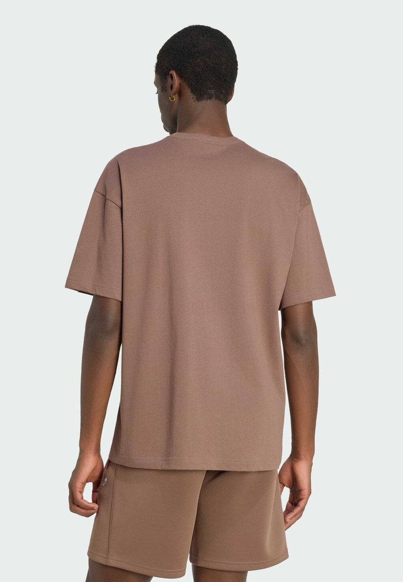 Homme portant un t-shirt marron à manches courtes ample et un short assorti, debout de dos devant un fond uni.