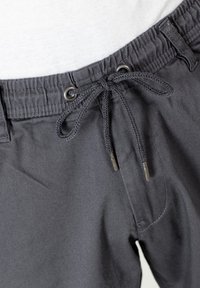 Pantalones cortos elásticos de talle alto en gris oscuro con cordón, que presentan ojales de metal y una tela texturizada. Primer plano de la cintura y detalles de costura.