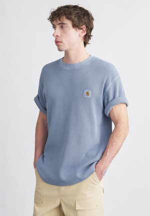 Hellblaues kurzärmliges T-Shirt mit strukturiertem Waffelmuster und einem kleinen quadratischen Logo-Patch auf der Brust.