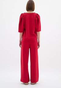 Červený dvoudílný outfit skládající se z topu s krátkým rukávem a nabíranými rukávy a širokých kalhot, vyrobený z hladkého materiálu v jednobarevném provedení.