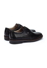 Chaussures habillées en cuir noir avec une texture lisse, un bout rond et un détail de laçage. Elles présentent un talon bas et une semelle marron contrastante.