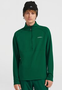 Grüner Reißverschluss-Pullover aus weichem Stoff, mit langen Ärmeln und Halbkragen. Er hat ein weißes Logo auf der Brust und ein enganliegendes Design.
