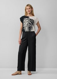 Combinaison noire et crème avec un imprimé feuillage sur le haut, manches courtes et pantalon ample. Tissu lisse avec une coupe décontractée.