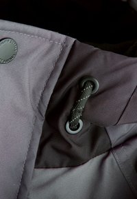 Tissu gris à texture lisse avec un œillet et un cordon de serrage noir, maintenu en place. Coutures visibles le long des bords.