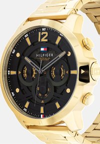 Montre en acier inoxydable doré avec un cadran noir texturé, trois sous-cadrans et de grands index horaires dorés, offrant une résistance à l'eau.