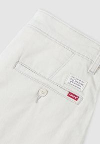 Poche arrière blanche du pantalon Levi's avec fermeture bouton, passants visibles pour ceinture et étiquettes de marque Levi's rouges et blanches.