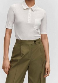 Polo blanc à côtes avec des manches courtes et une patte de boutonnage, associé à un pantalon taille haute vert olive. Tissu texturé, détail de poche.
