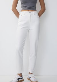 White denim pants with a straight-leg cut, featuring side pockets and a button closure. Paired with gray top and sneakers, against a neutral background.